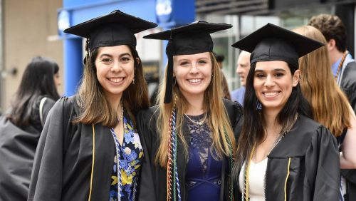 Three female students posing for a picture and dressed in graduation gowns and caps.