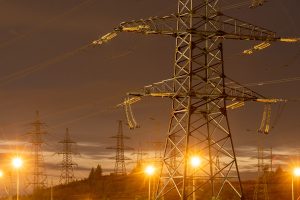 A night-time view of multiple illuminated electricity pylons and power lines against a dusk sky.