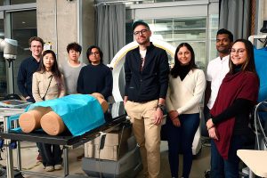 Mathias Unberath, and 7 members of his lab pose for a photo next to a dummy and an imaging machine.